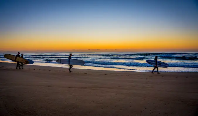 Surfers walking down the beach at sunset with their surfboards