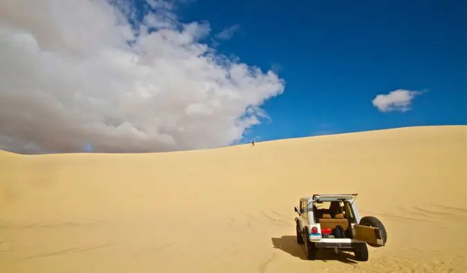 A rented car exploring the sand dunes in Africa under a bright blue sky
