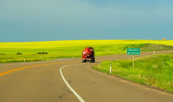 Red truck on an open road with a green feild in the countryside