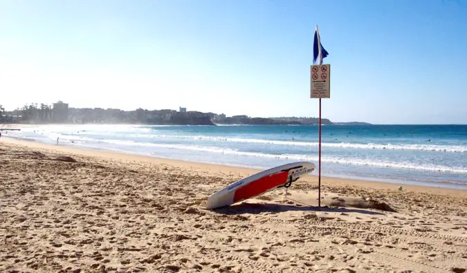A lone surfboard resting in the sand on the stunning Manly Beach